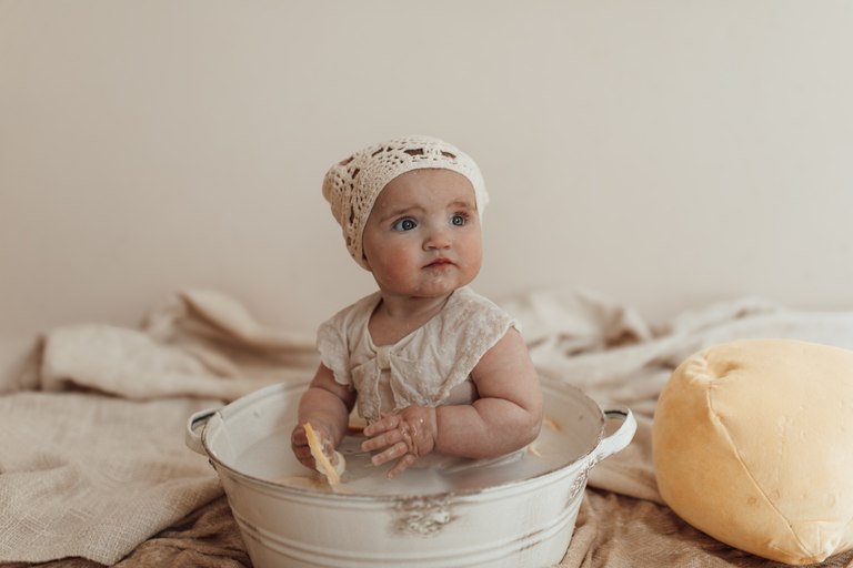 Baby mit Häubchen in einem Milchbad mit Zitrusfrüchten