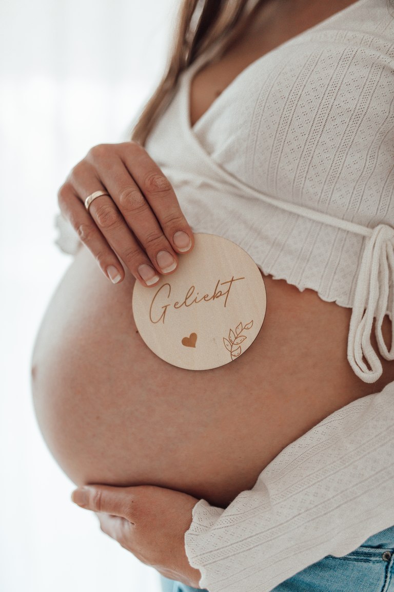 Hände am Babybauch mit einem Holzschild Geliebt